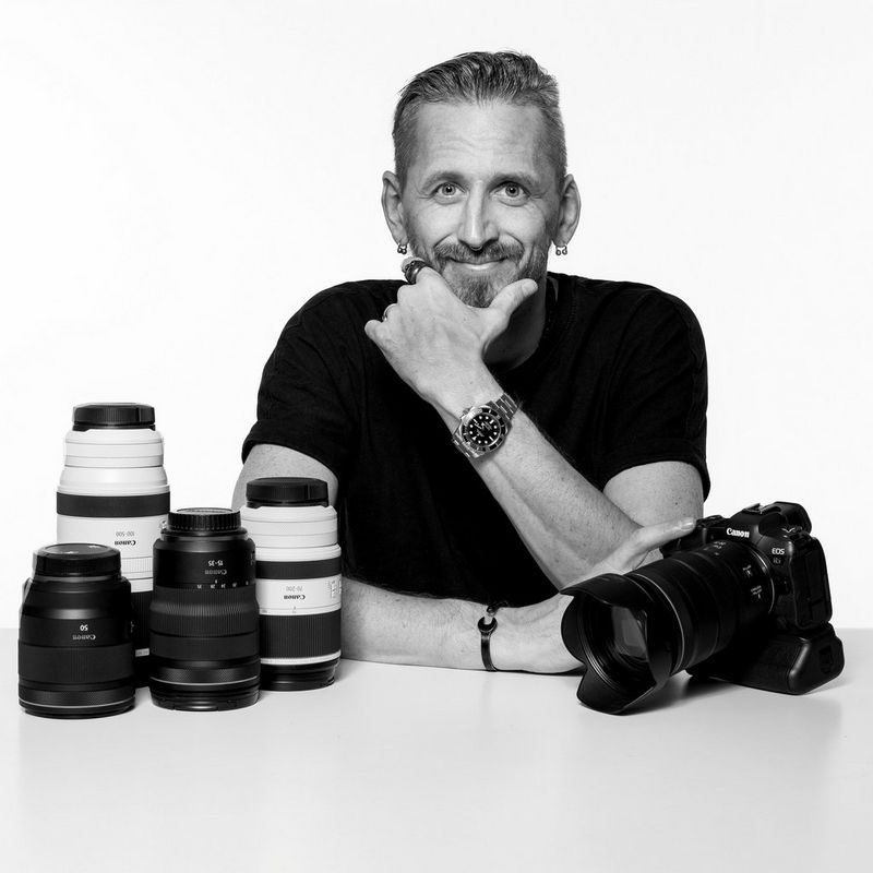 A black and white portrait of Canon Ambassador Tomáš Třeštík, seated behind a Canon camera and lenses.