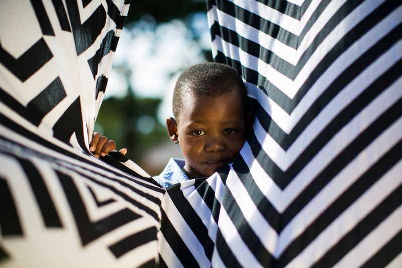 A child plays hide and seek in the sheets of the weekly wash at an orphanage in Malawi. Taken on a Canon EOS 5D Mark III by Canon Ambassador Tristan Schäfer.