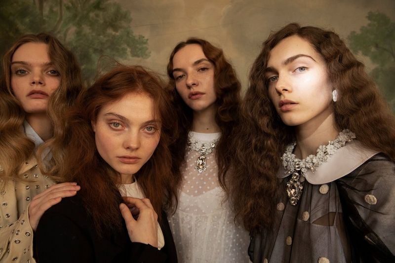 Four young women standing posed in front of a landscape painting.