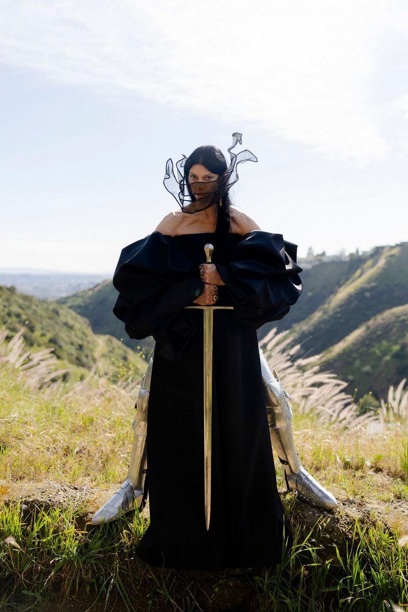 A portrait of a woman in a voluminous black dress and with a veil obscuring her face holding a large sword.