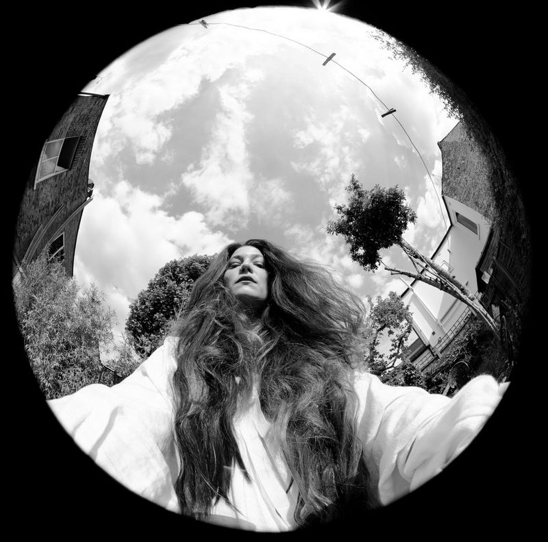 A black-and-white self-portrait of a woman in a back garden taken with a fisheye lens.