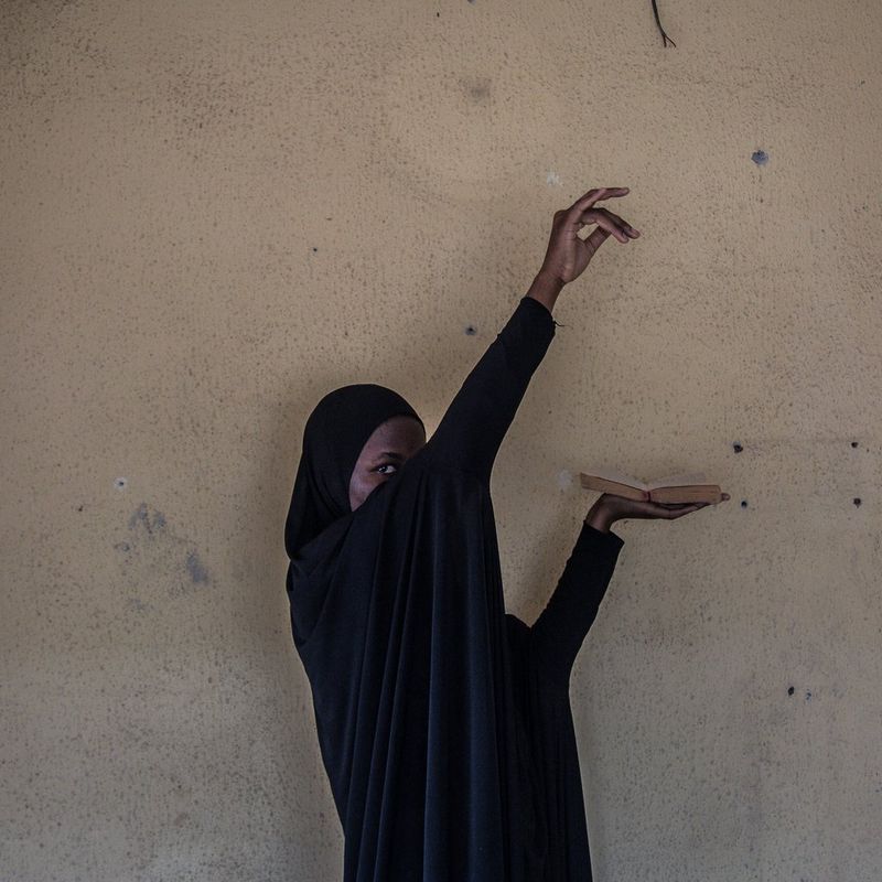 A woman covers her face with her arm and holds her hands up high while being photographed.