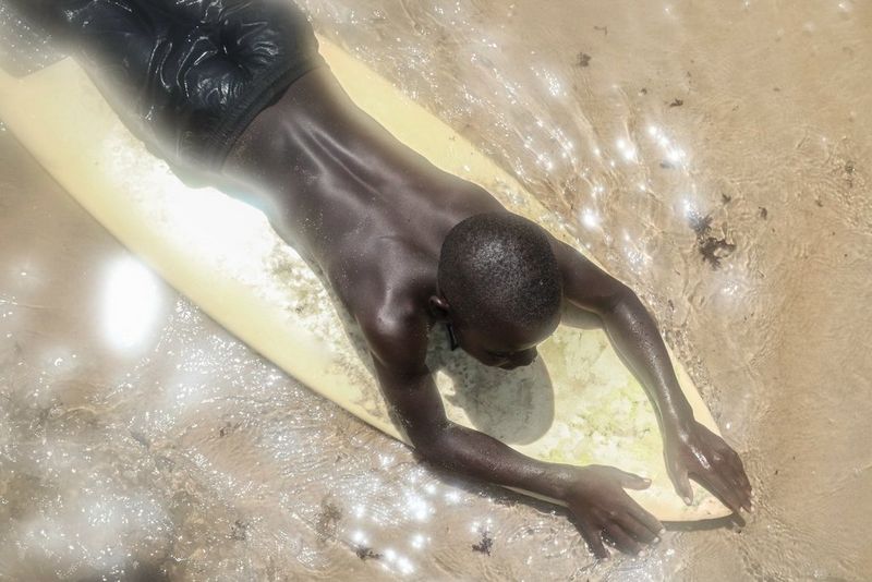 A man lies on a surfboard in the shallow waters of a beach. 