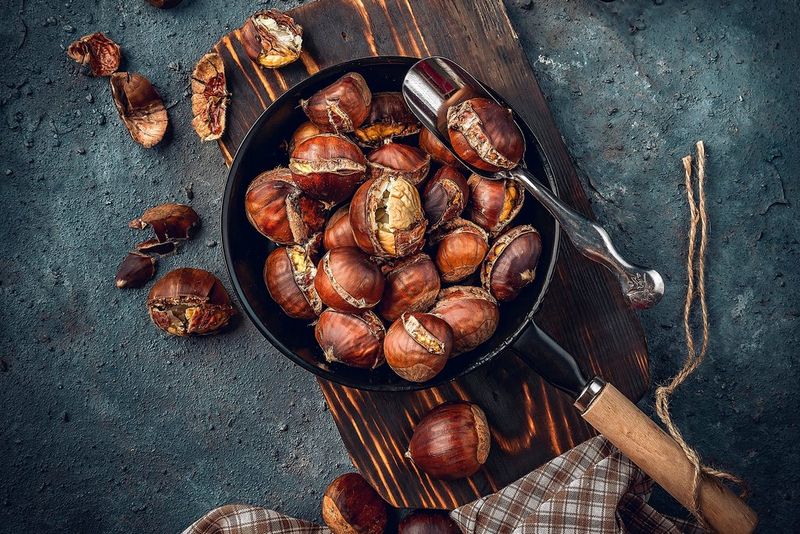 Roasted chestnuts in a frying pan on a wooden chopping board.