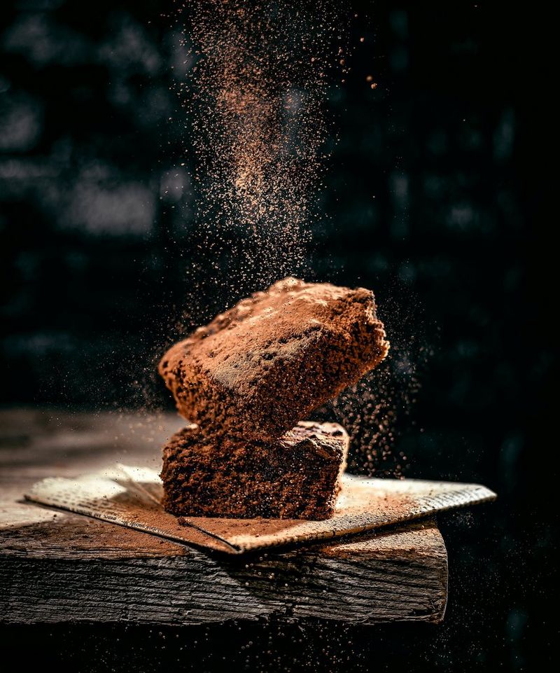 A dusting of powdered chocolate falls onto two squares of chocolate brownie. 