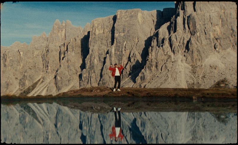 AntsLive стоит перед каменистым холмом возле своего отражения в водоеме; кадр из видео на песню Number One Candidate.