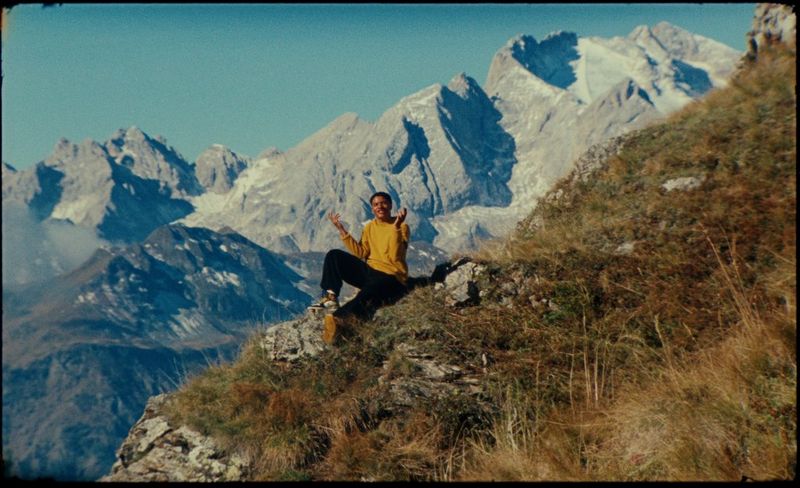 AntsLive сидит на травянистом склоне, а на фоне виднеются другие горные вершины.