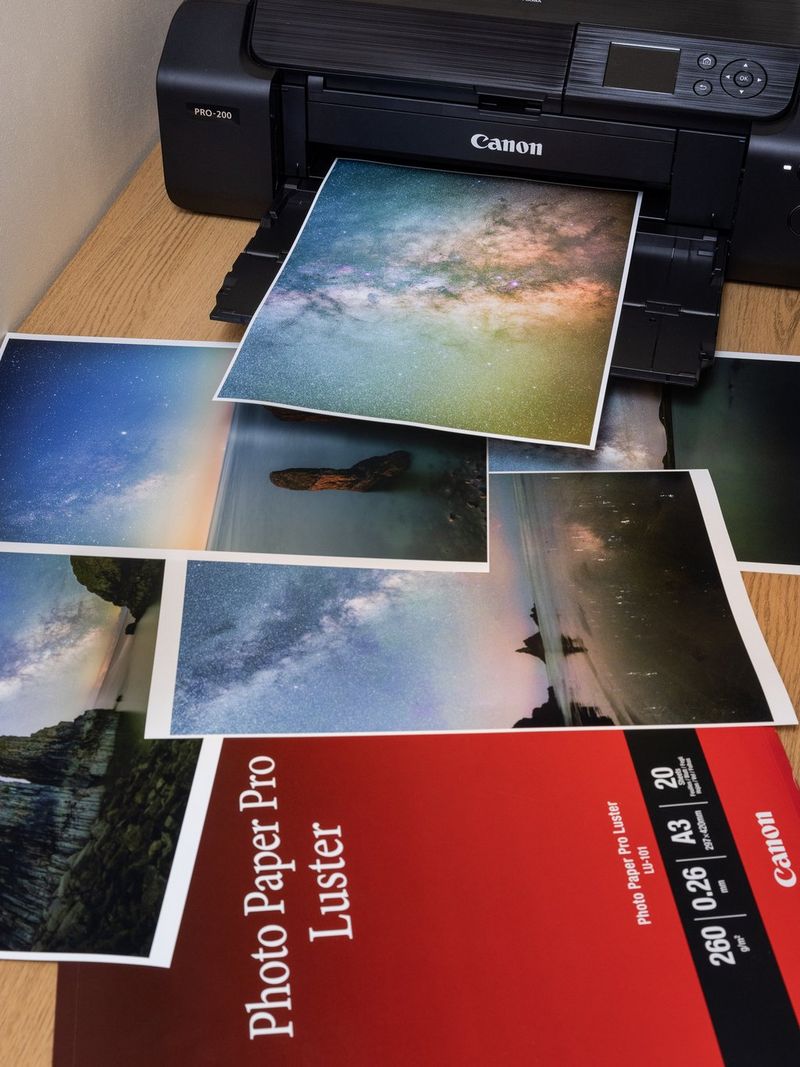 Een selectie astrofotografieprints die voor een Canon-printer liggen en uit de printer komen, naast een pak printerpapier van Canon.