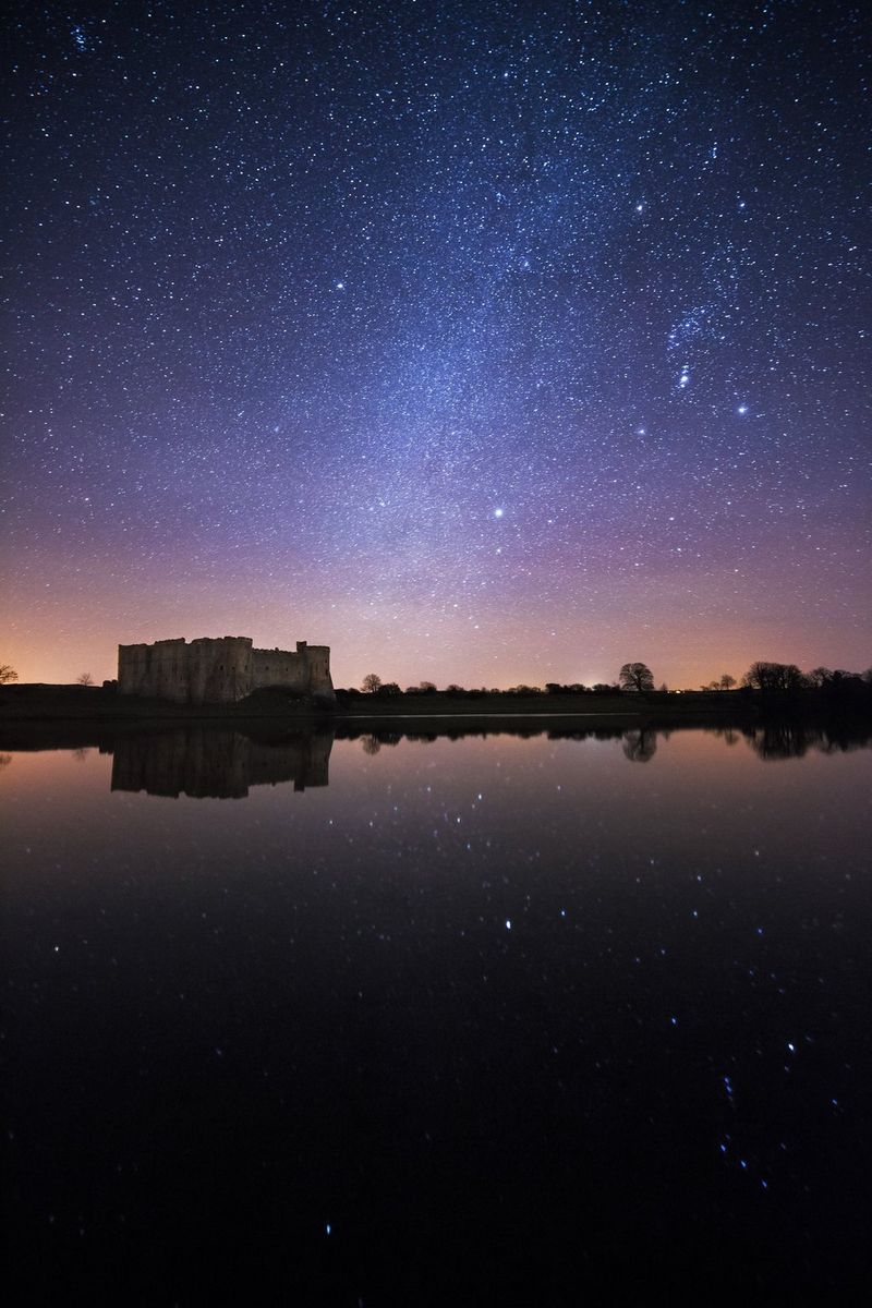 Een roze en paars gekleurde nachtelijke hemel vol sterren boven Carew Castle in Pembrokeshire, Wales.
