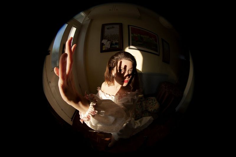 Un autoritratto con obiettivo fisheye di Wanda Martin con un top a spalle scoperte svolazzante che tiene la mano alzata lateralmente verso l'obiettivo.