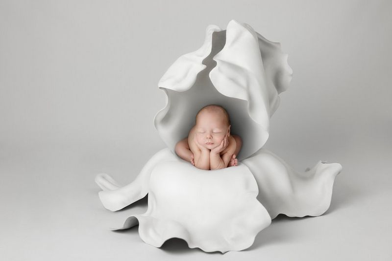 A baby rests their hands under their chin as they sleep inside a large white flower in a photograph by Kelly Brown taken on a Canon EOS R5.
