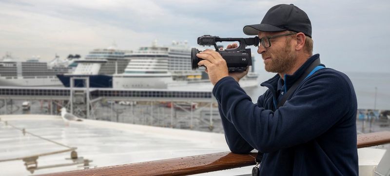 Clemens Boecker filming with a Canon XA55, with large cruise ships in the background.