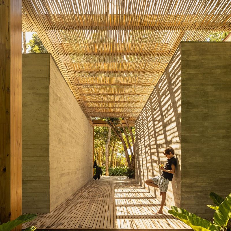 A figure leans against a wall, slats on the wooden overhang creating light patterns below.