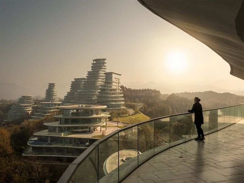 A figure stands on a curved balcony overlooking the city.