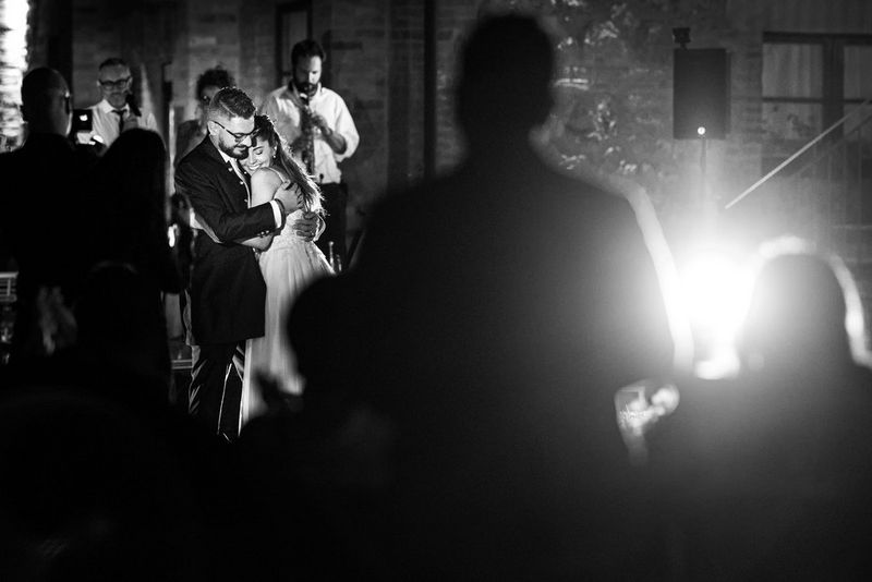 Un'immagine in bianco e nero di uno sposo e una sposa al loro primo ballo. Sono circondati da persone che scattano fotografie.