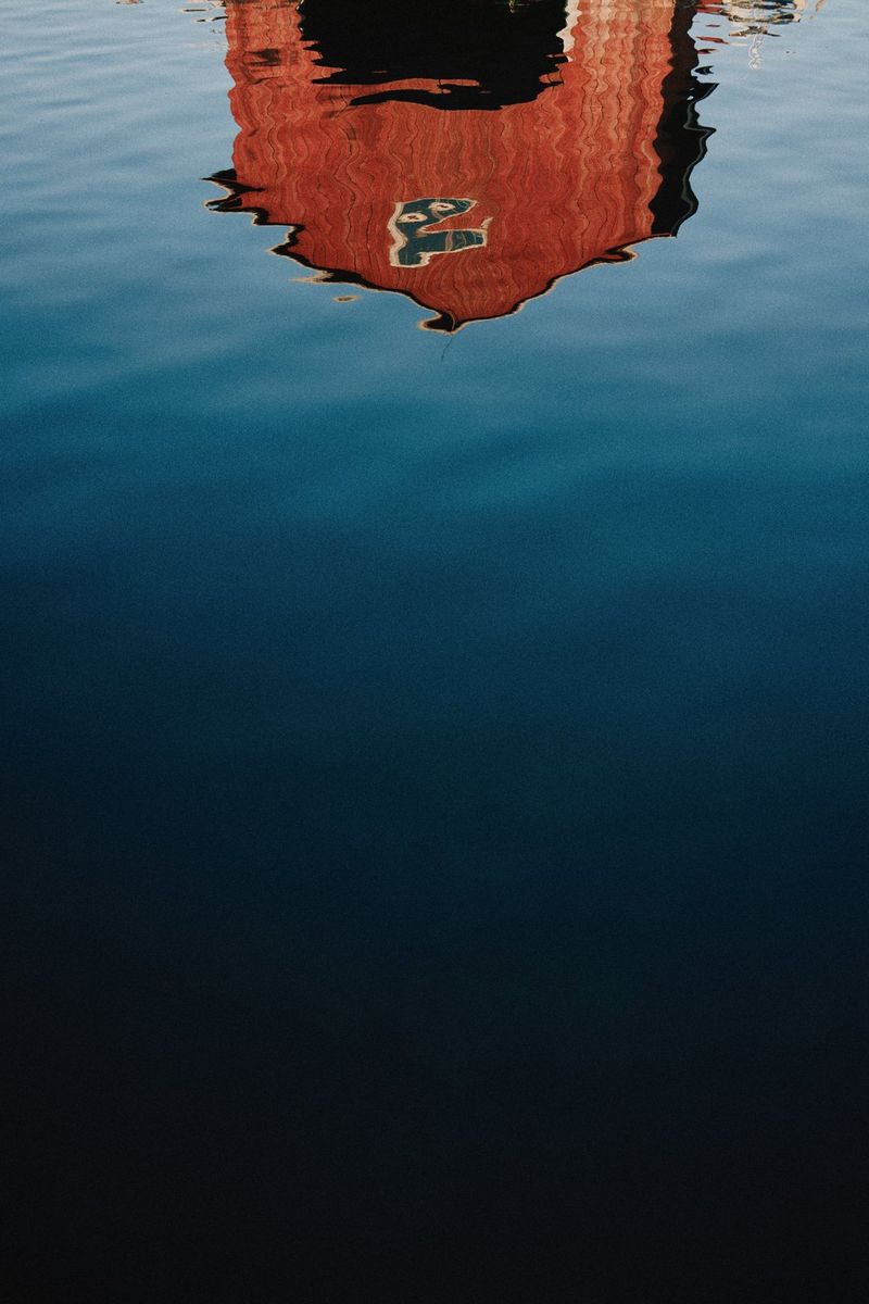 Небольшое строение отражается в поверхности воды, которая немного идет рябью, в результате чего отражение теряет форму.