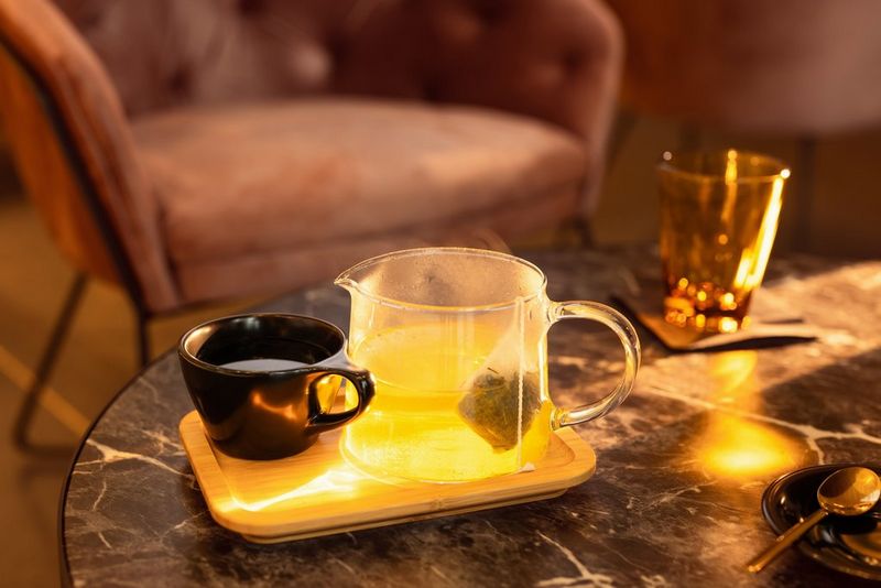 A promotional shot showing a glass pitcher of tea and a small black cup set atop a small tray on a marbled coffee table.