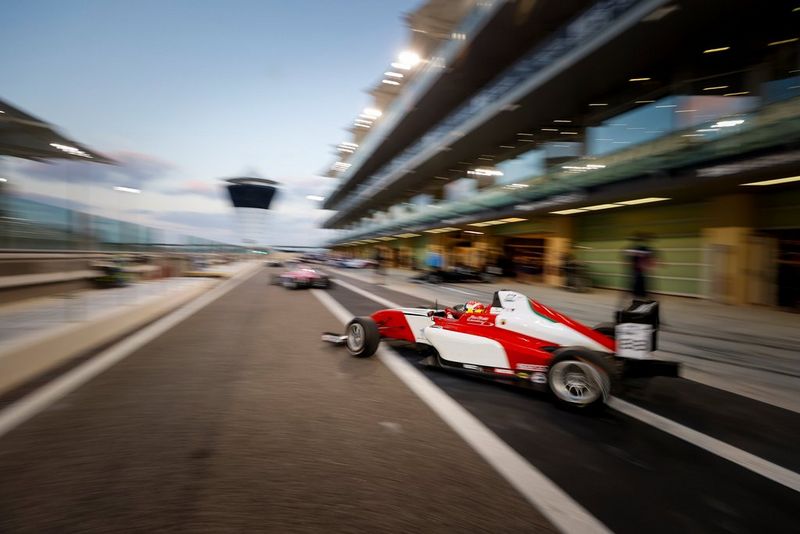Красно-белый болид выезжает на трассу. Камера поворачивается, следуя за ним, а фон получается размытым благодаря выбору длительной выдержки.