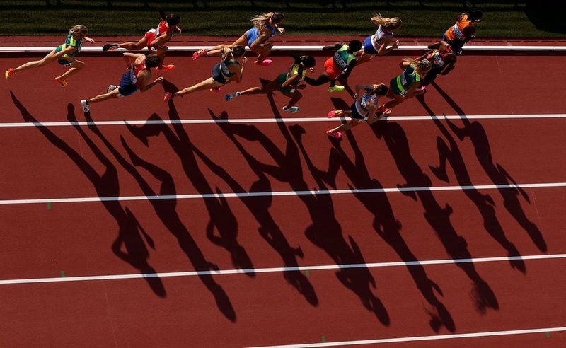Des sprinteuses courent sur une piste d'athlétisme, leurs ombres s'étirant sous elles. Photo prise avec un Canon EOS R3 équipé d'un objectif Canon RF 100-300mm F2.8L IS USM.