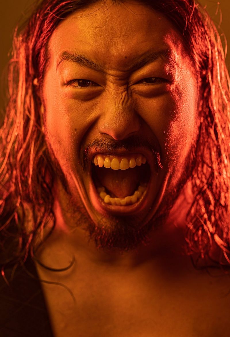 Окутанный красным светом человек открыл рот в попытке изобразить рык и смотрит прямо в камеру; портрет, созданный Джеймсом Масселуайтом с помощью объектива Canon RF 100mm F2.8L MACRO IS USM.