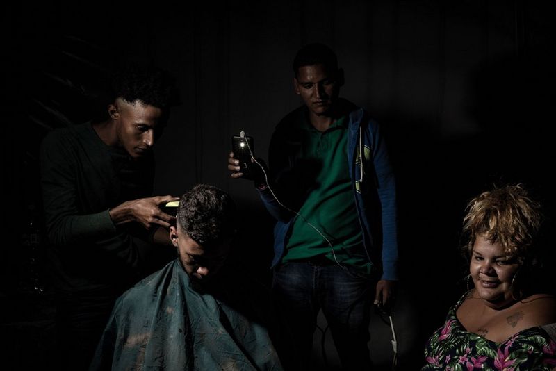 Мужчину стригут при свете фонарика телефона.