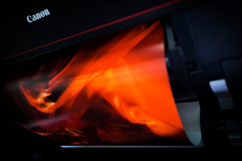 Принтер Canon PROGRAF с модулем рулонной подачи печатает изображение женщины в огненно-красной шали.