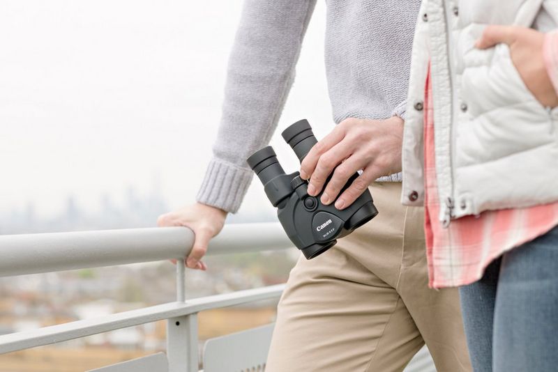  A young couple in bright clothing looking out over a cityscape. The man is holding a pair of Canon 10x30 IS II binoculars.