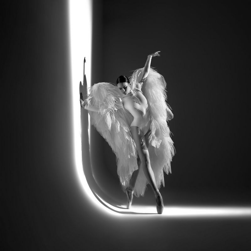 Una ballerina, che indossa delle grandi ali di piume bianche, è in posa davanti allo sfondo di uno studio fotografico in uno scatto di Sascha Hüttenhain, realizzato con fotocamera Canon EOS R5 e obiettivo Canon RF 24-70mm F2.8 L IS USM.