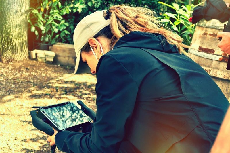 Regisseur Basha de Bruijn zit op een filmset en draagt een jack en honkbalpet, terwijl ze gemaakte beelden bekijkt op een scherm.