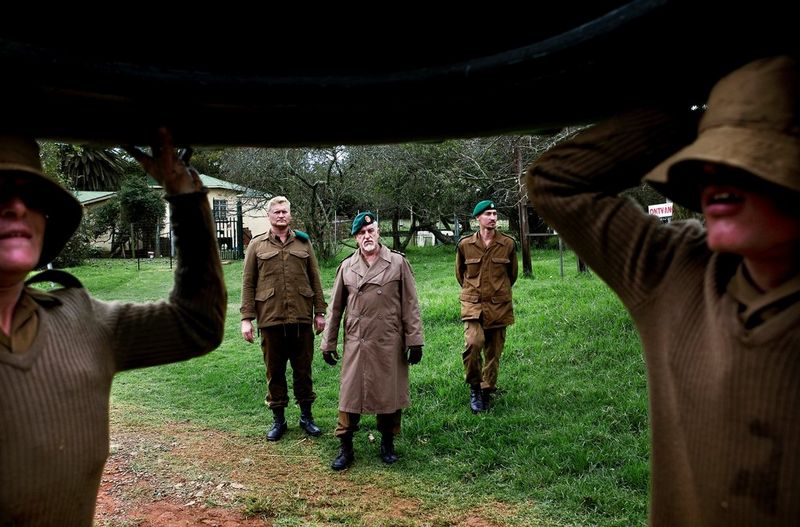 In un campo giovanile sudafricano, due persone trasportano uno pneumatico mentre tre uomini osservano, in uno scatto di Ilvy Njiokiktjien.