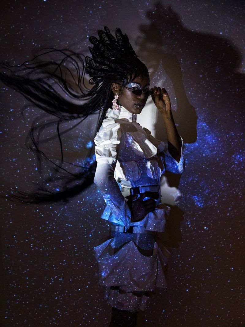 A woman with an elaborate hairstyle with an image of the night sky projected onto her, meaning that only her face and torso are clearly visible.