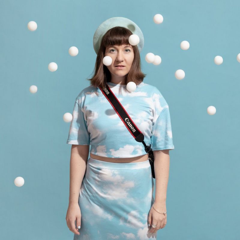 Canon Ambassador Eliška Sky against a sky blue background that matches her clothes, with table tennis balls in the air around her. 