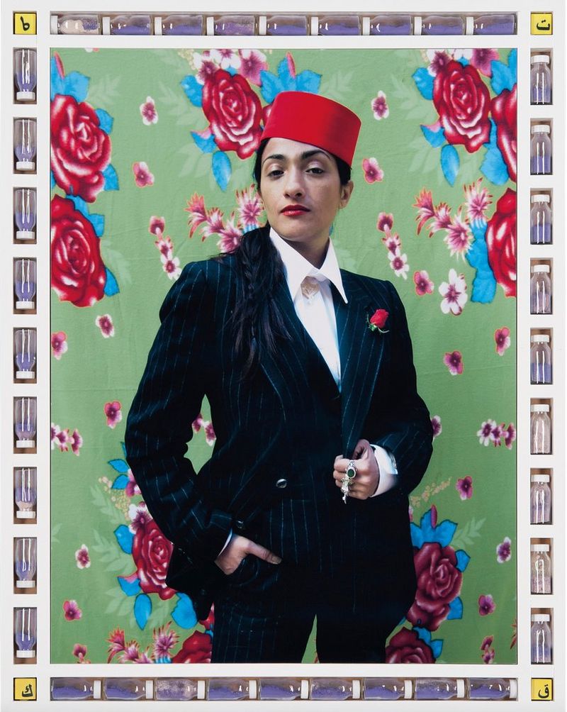 A woman in a suit wearing a fez, standing in front of a painted background of large red roses. The image's frame is composed of plastic bottles of a blue substance. 