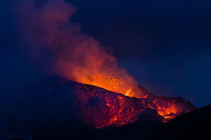 Oranje lava en rook rijzen de donkerblauwe lucht in boven een uitbarstende vulkaan.