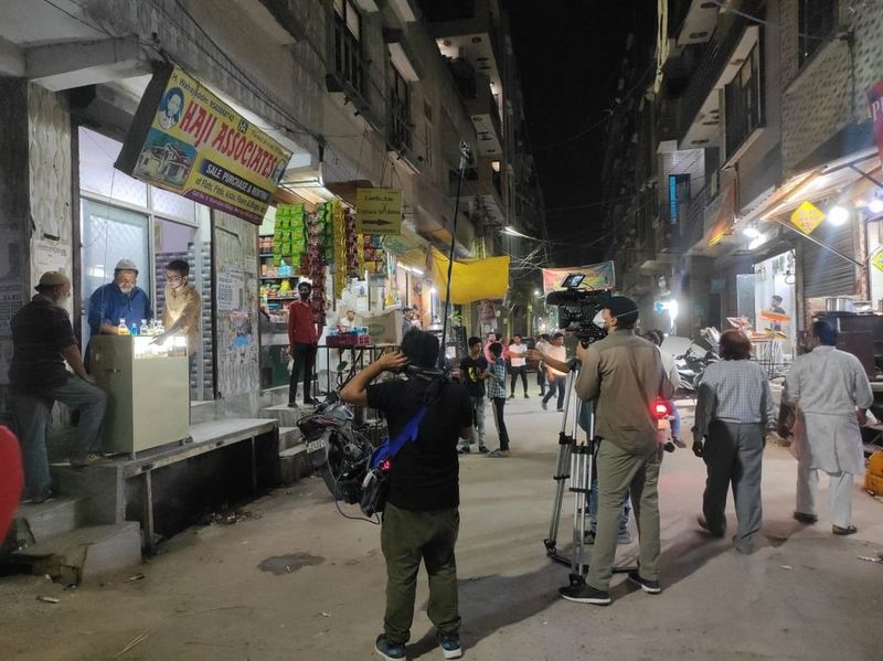 A film crew stands in a busy Delhi side street capturing the local environment.