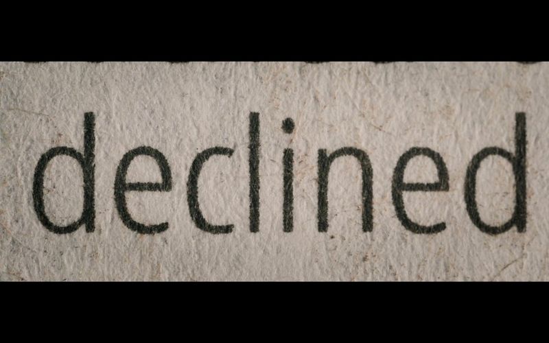 A close-up of the word "declined" on a sheet of white paper, showing the texture of the paper and ink, filmed with a Canon MP-E 65mm f/2.8 1-5x Macro Photo lens.