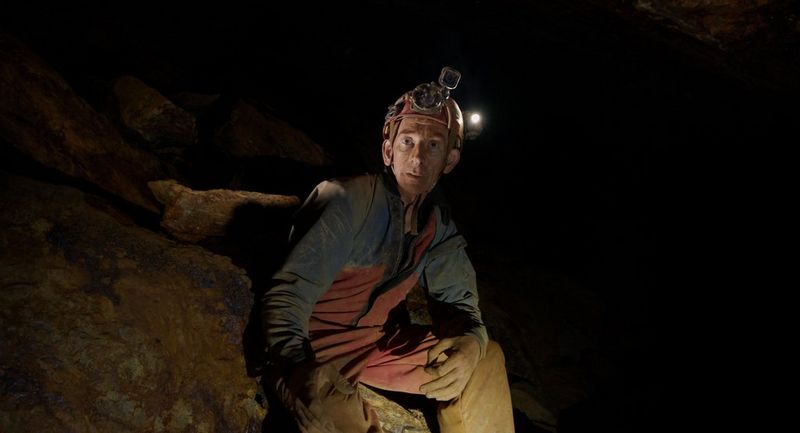A man in a dusty blue outfit and red helmet with attached head torch looks straight at the camera, in a still from Daniel Simpkins' current documentary project set in abandoned Cornish mines, captured on the Canon EOS C70 cinema camera.