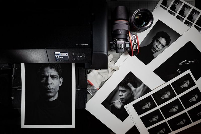 Een Canon imagePROGRAF PRO-300 print een portret van het gezicht en de schouders van een man. Naast de printer staan een Canon-camera en -objectief en liggen nog meer prints van dezelfde man.