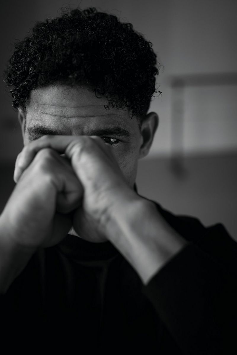 Een zwart-witportret van een man die zijn handen gevouwen voor zijn gezicht houdt.