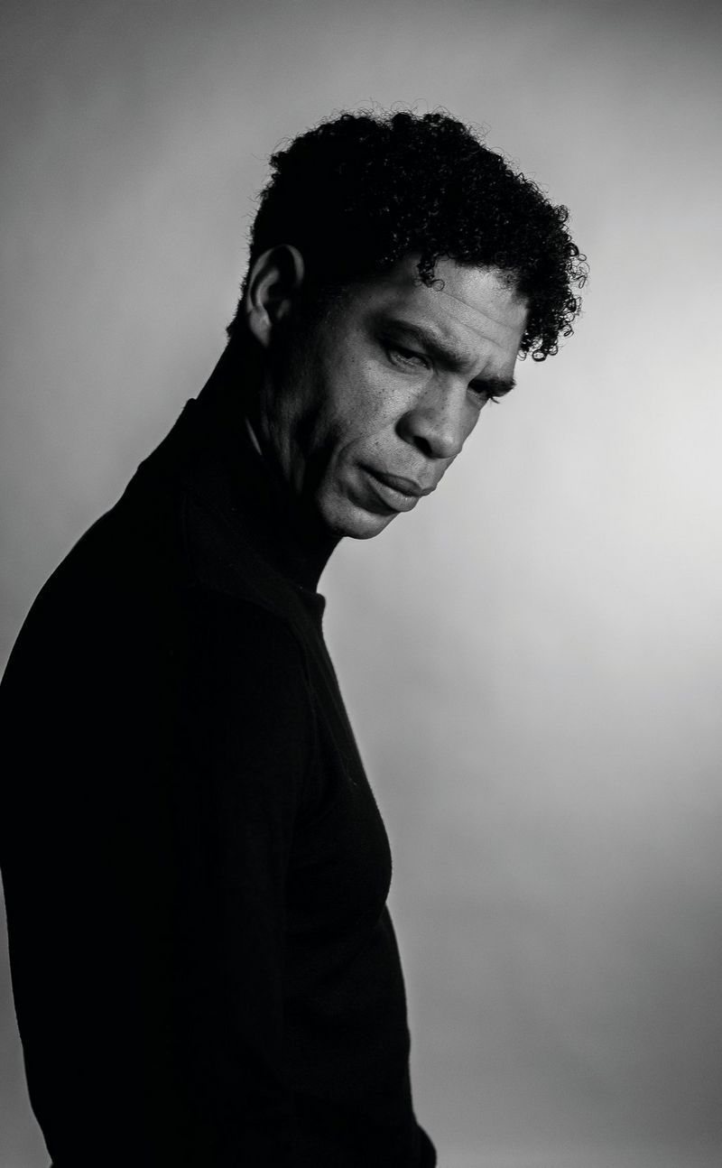 Een Canon imagePROGRAF PRO-300 print een zwart-witportret van een man in een zwart shirt en zwarte broek die op een stoel voor een raam poseert.