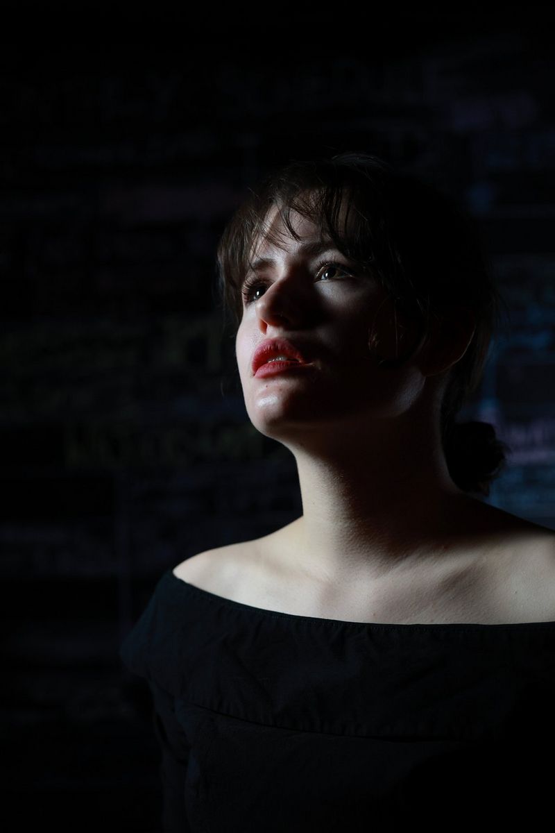 A portrait of a woman wearing an off-the-shoulder black top and looking up into the distance, photographed by Clive Booth.