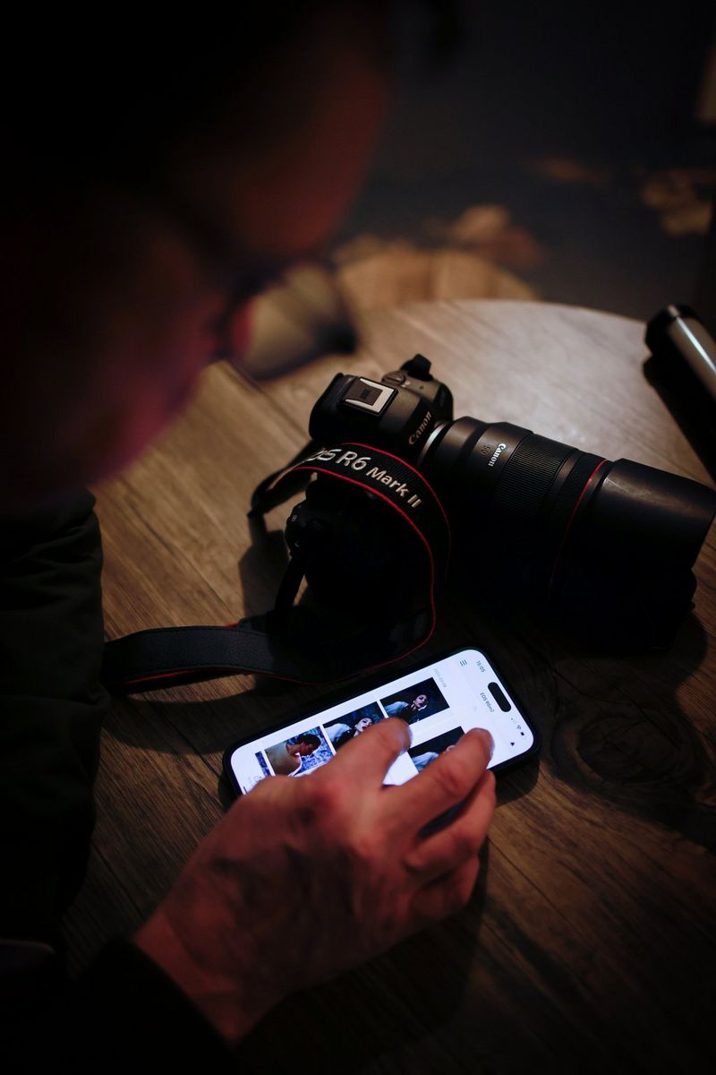 A man scrolls through photos on a smartphone. The photos were taken on a Canon EOS R6 Mark II which sits next to the smartphone on a table. 