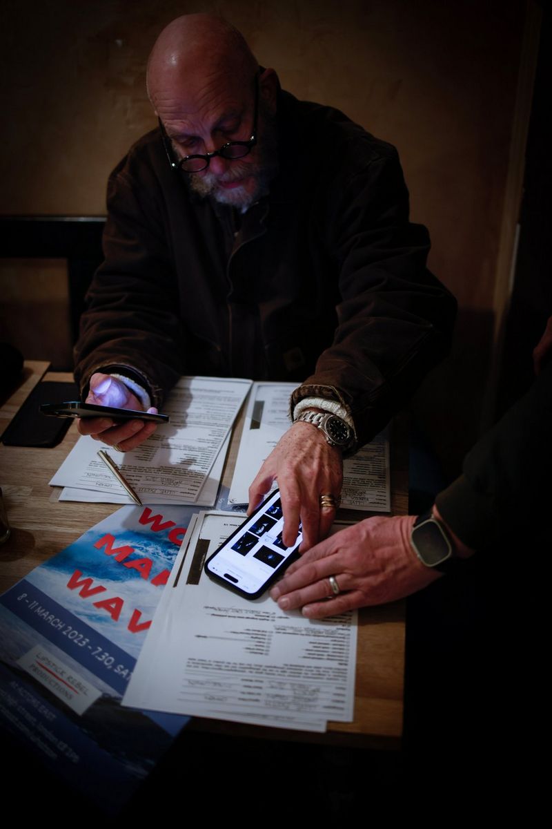 A man places a smartphone on a small pile of papers while holding another smartphone in his right hand.