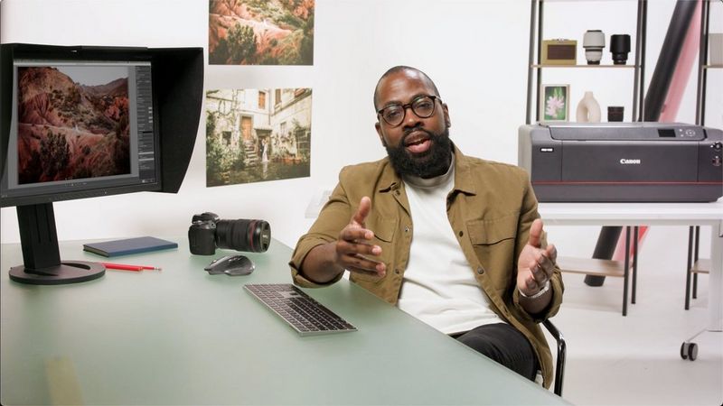 Photogapher Igor Demba sits at a desk with a monitor displaying a landscape image, and a Canon imagePROGRAF PRO-110 printer in the background.