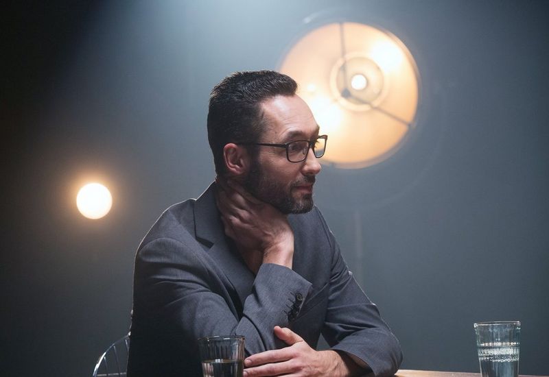 A side profile of Thomas Borberg; he is sat in front of a studio light with his hand resting on his neck.