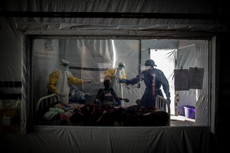 An Ebola patient is treated in an isolation pod by three medics wearing medical gowns and face masks.