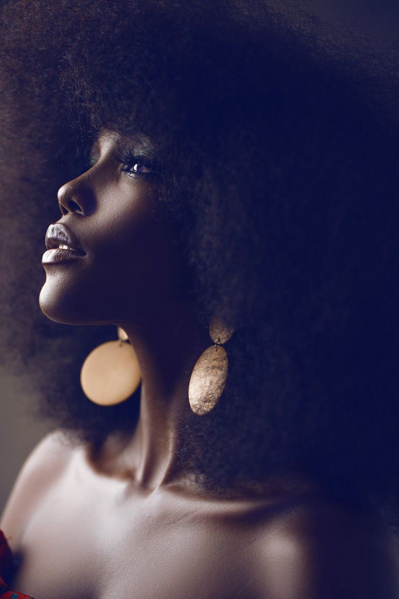 Un primo piano di una donna, girata quasi di profilo e con lo sguardo rivolto verso l'alto. Il suo viso è incorniciato da capelli folti e sciolti e indossa orecchini pendenti con dischi d'oro. Scatto realizzato da Emmanuel Oyeleke con una fotocamera Canon EOS R.