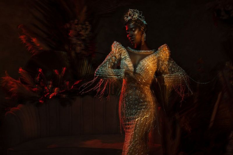 Una donna con indosso un elaborato abito di perline a spalle alte e una tiara scintillante mentre balla, con scie che mostrano il movimento delle braccia e del vestito. Scatto realizzato da Emmanuel Oyeleke con Canon EOS R5.