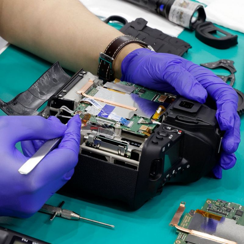  A technician wearing purple gloves works on the circuitry of a Canon camera on a table.