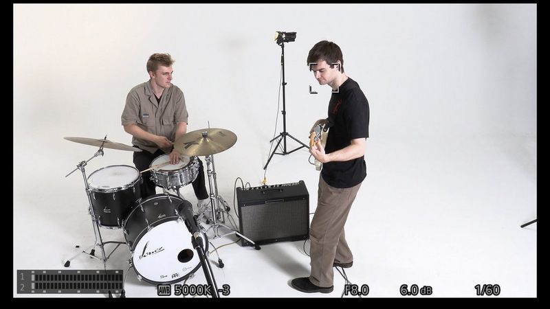 A PTZ camera's view of a drummer and guitarist performing, with a face tracking AF frame on the face of the latter.